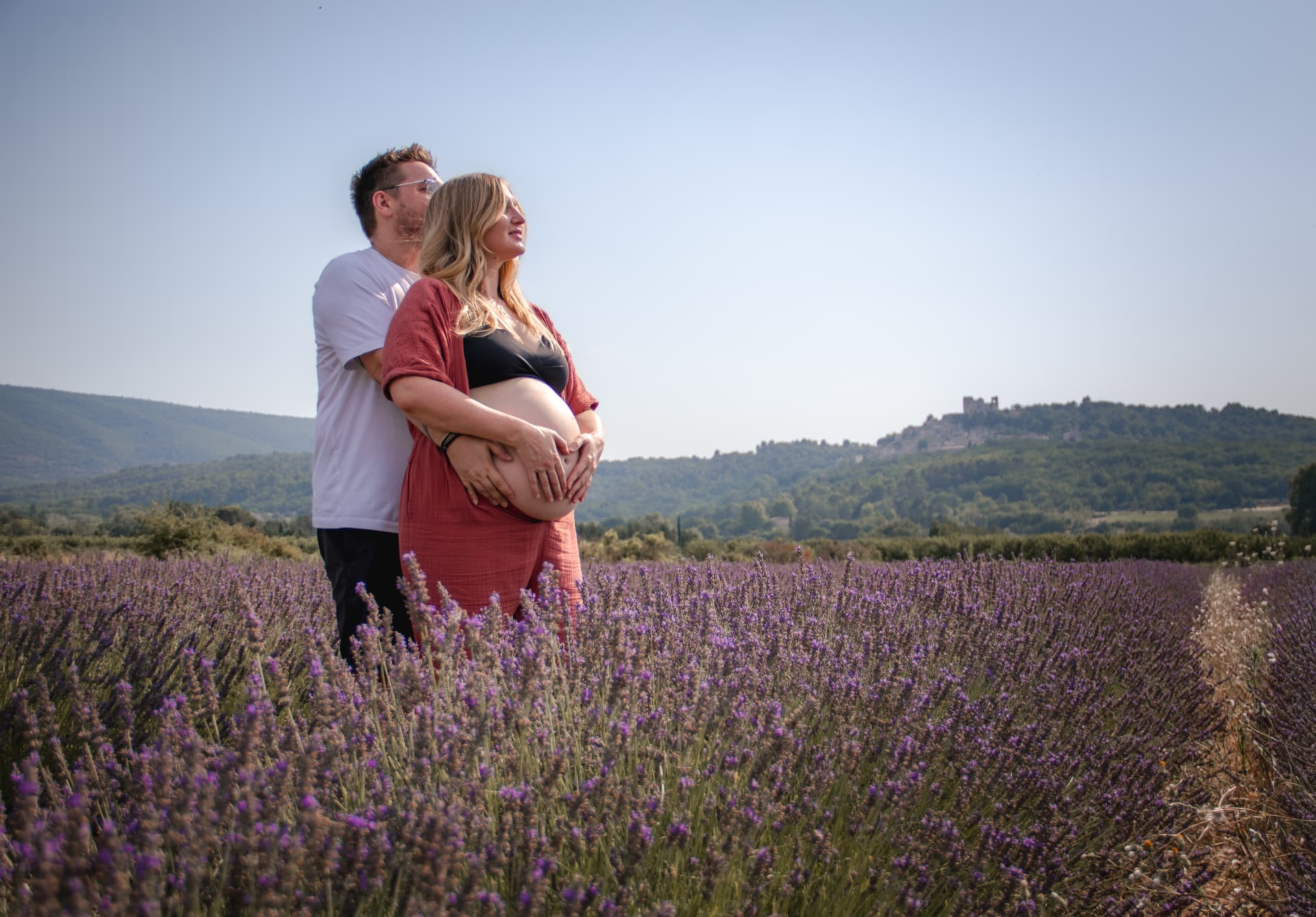Seance photo grossesse champ de lavande Provence, couple enlacé devant un village perché