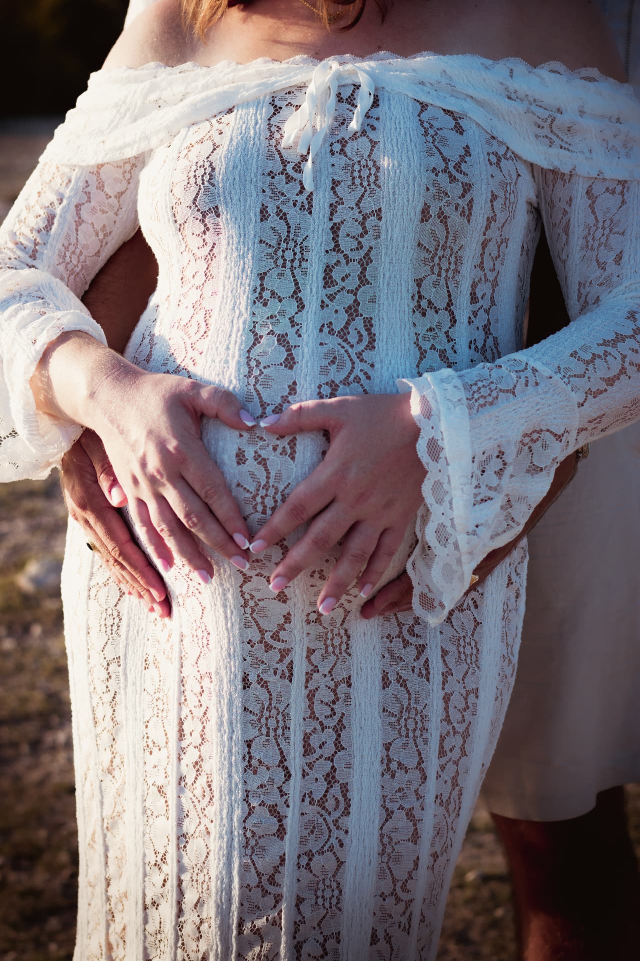 Mains des futurs parents formant un cœur sur le ventre en robe de dentelle