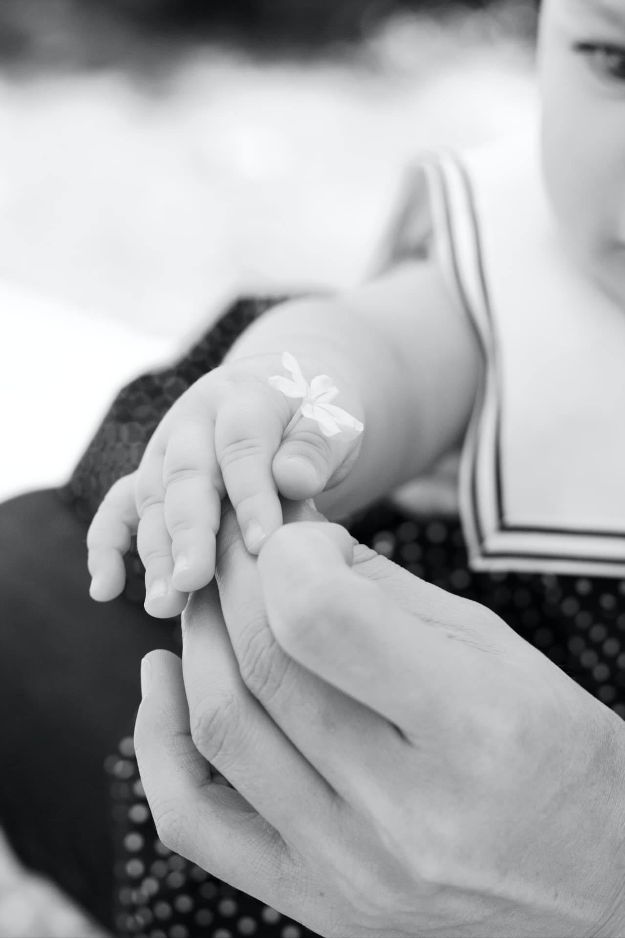 Main de nouveau-né tenant une petite fleur blanche, séance naissance en noir et blanc