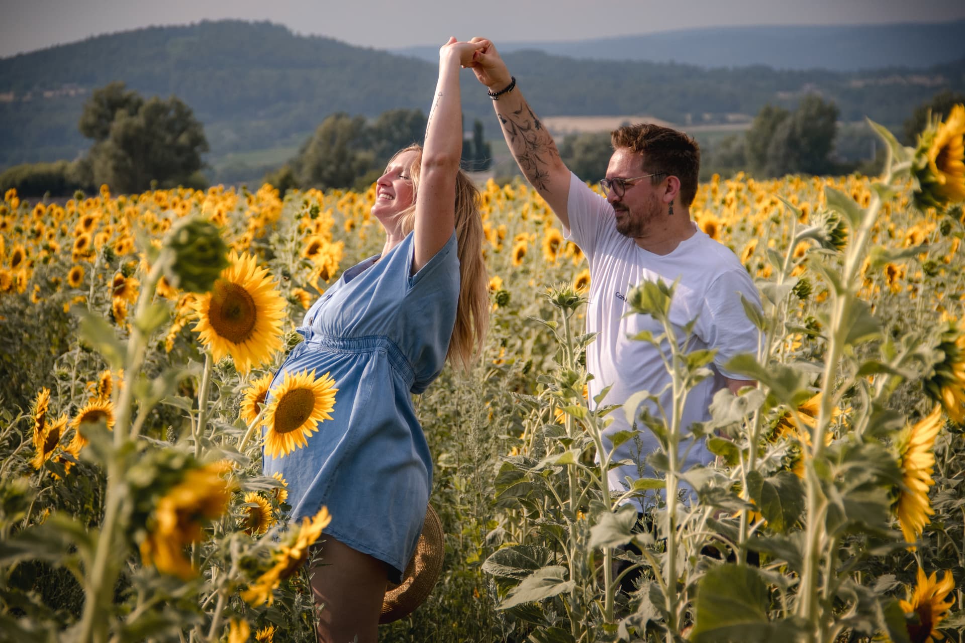 Future maman dansant avec son compagnon dans un champ de tournesols