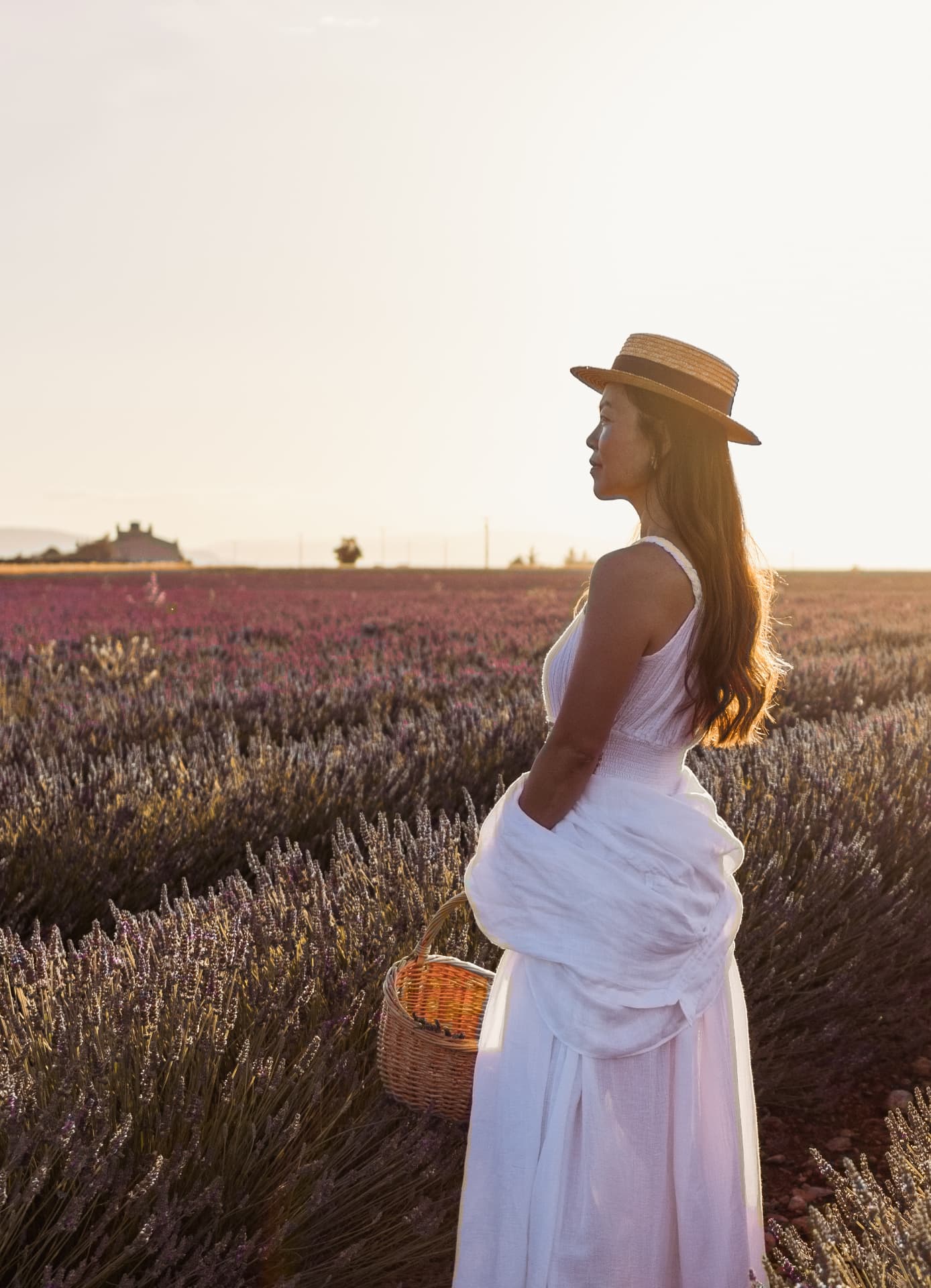 Femme en robe blanche et chapeau de paille dans un champ de lavande au coucher du soleil