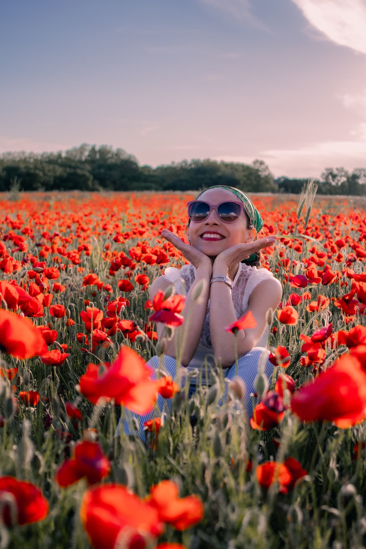 Femme souriante assise au milieu des coquelicots au coucher du soleil