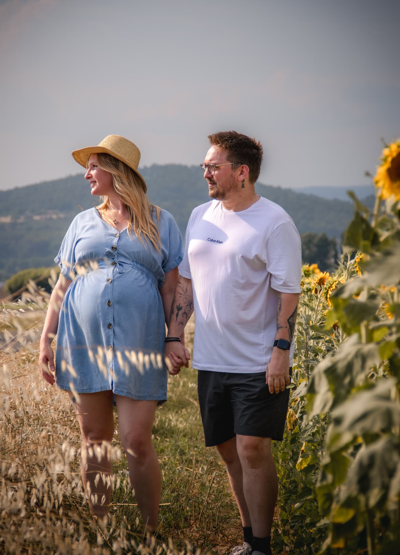 Couple attendant un bébé main dans la main près d'un champ de tournesols en Provence
