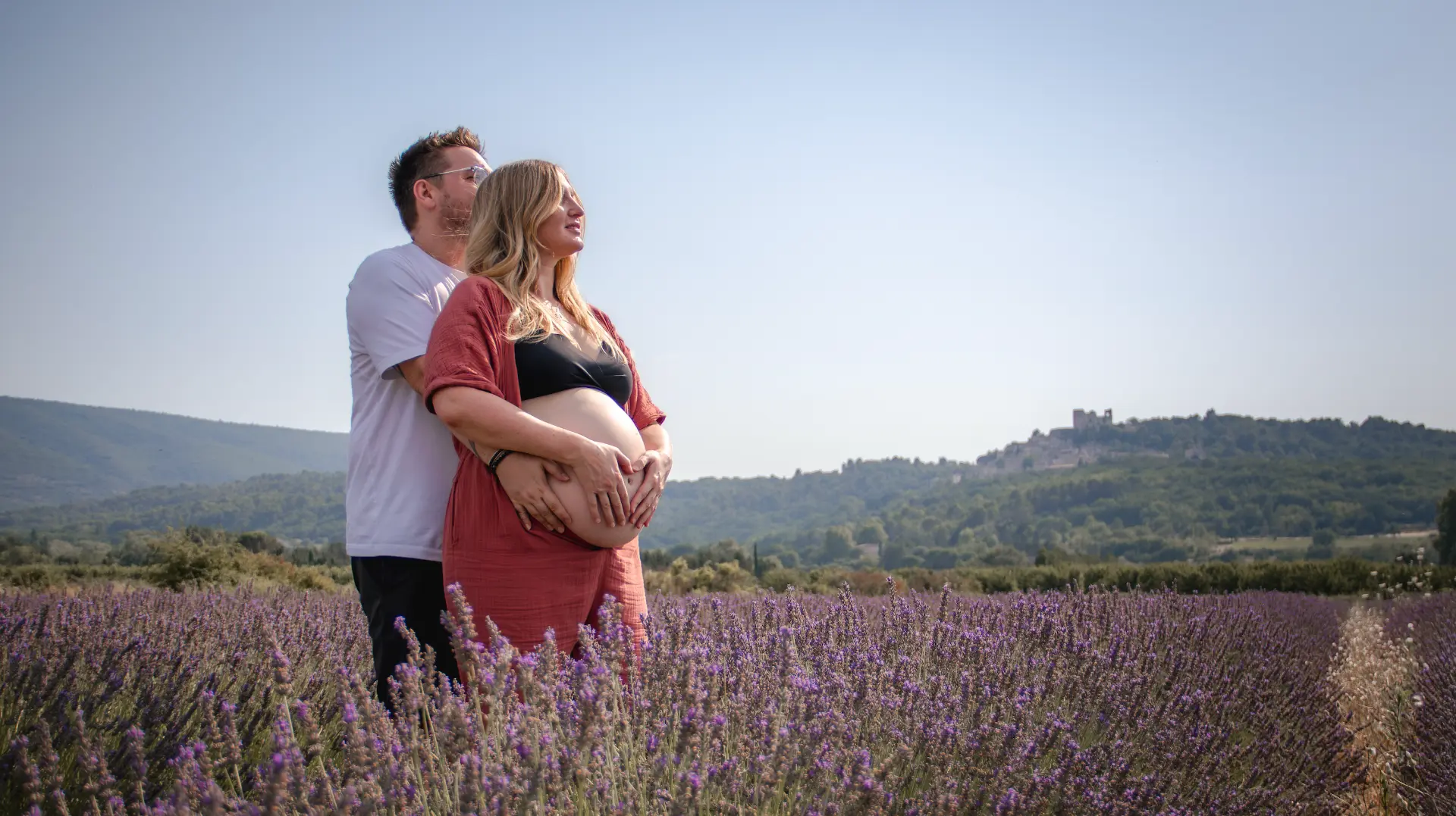 Futurs parents dans un champ de lavande face à un village perché
