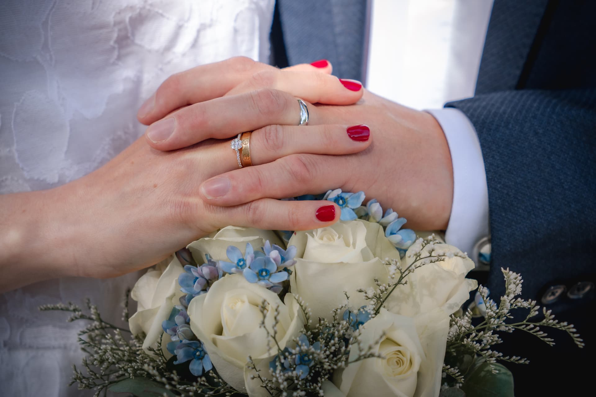 Mains des mariés et alliances posées sur un bouquet de roses blanches